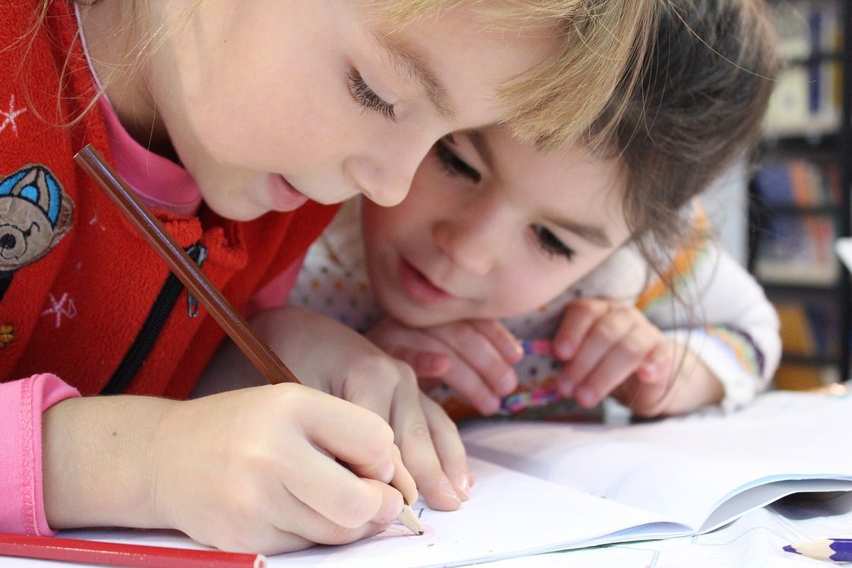 Un enfant tenant un crayon pour dessiner et un autre qui le regarde faire